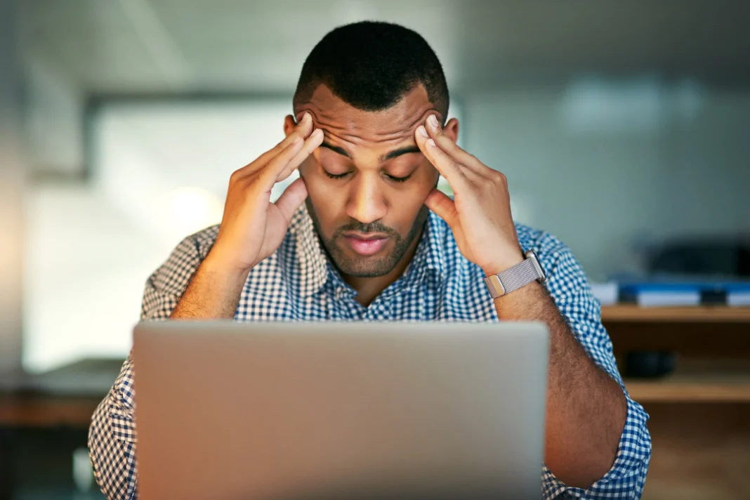 man holding his head in front of laptop