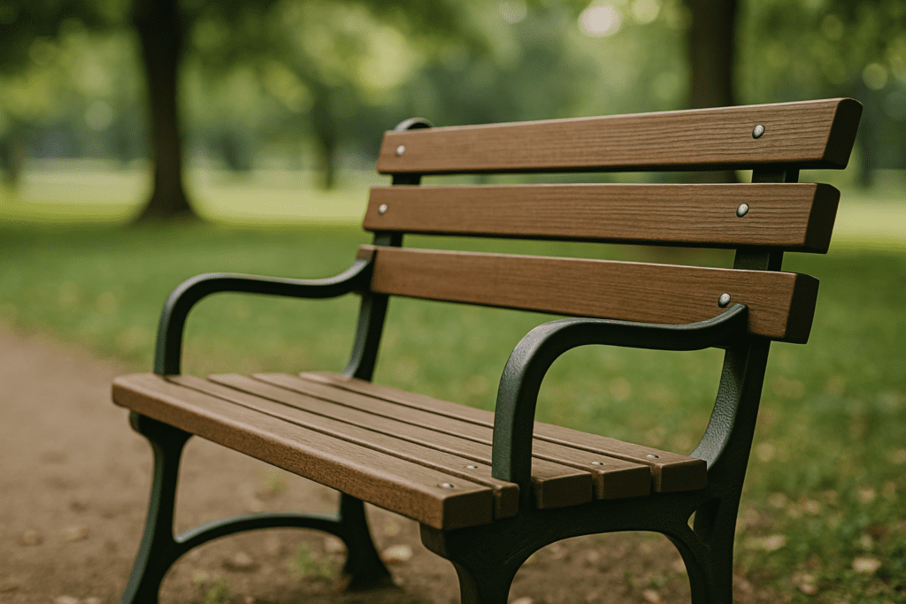 Empty wooden park bench with iron armrests placed along a quiet path, surrounded by blurred green trees in natural daylight