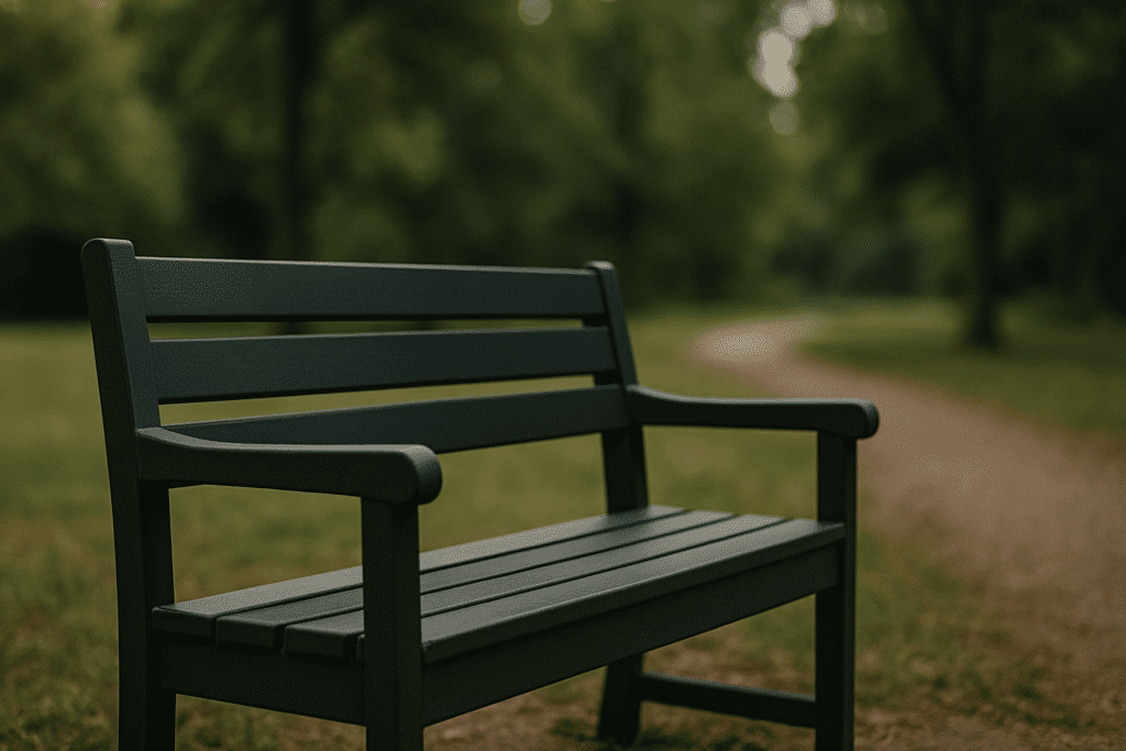 A dark green wooden park bench sits quietly along a gravel path in a leafy park, surrounded by softly blurred trees and natural light