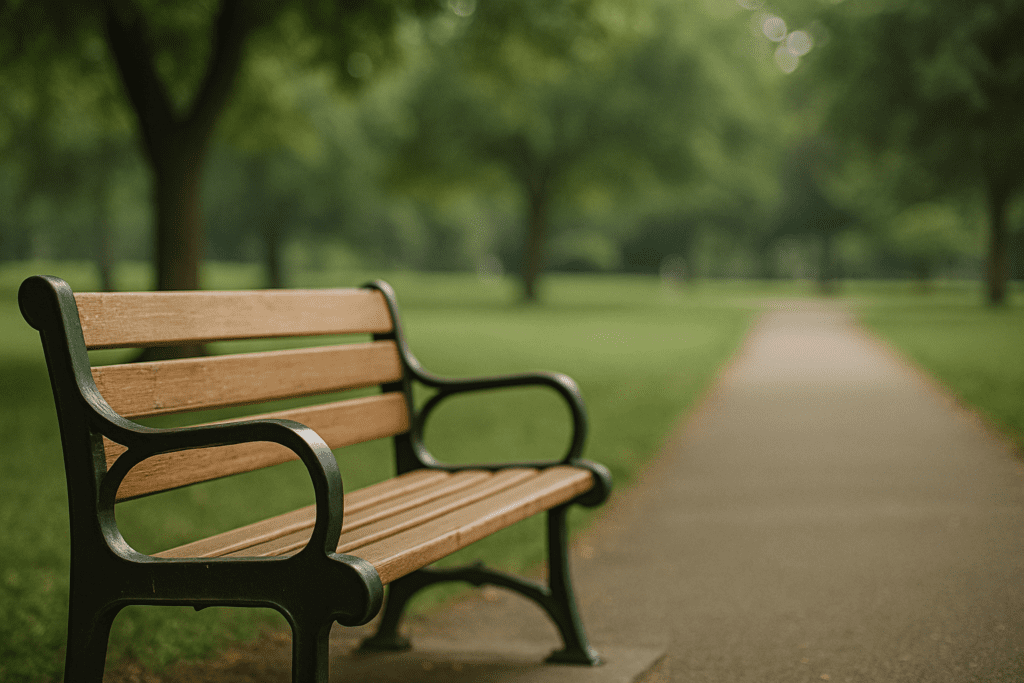 Empty wooden bench with a black metal frame sits beside a tree-lined path in a tranquil green park