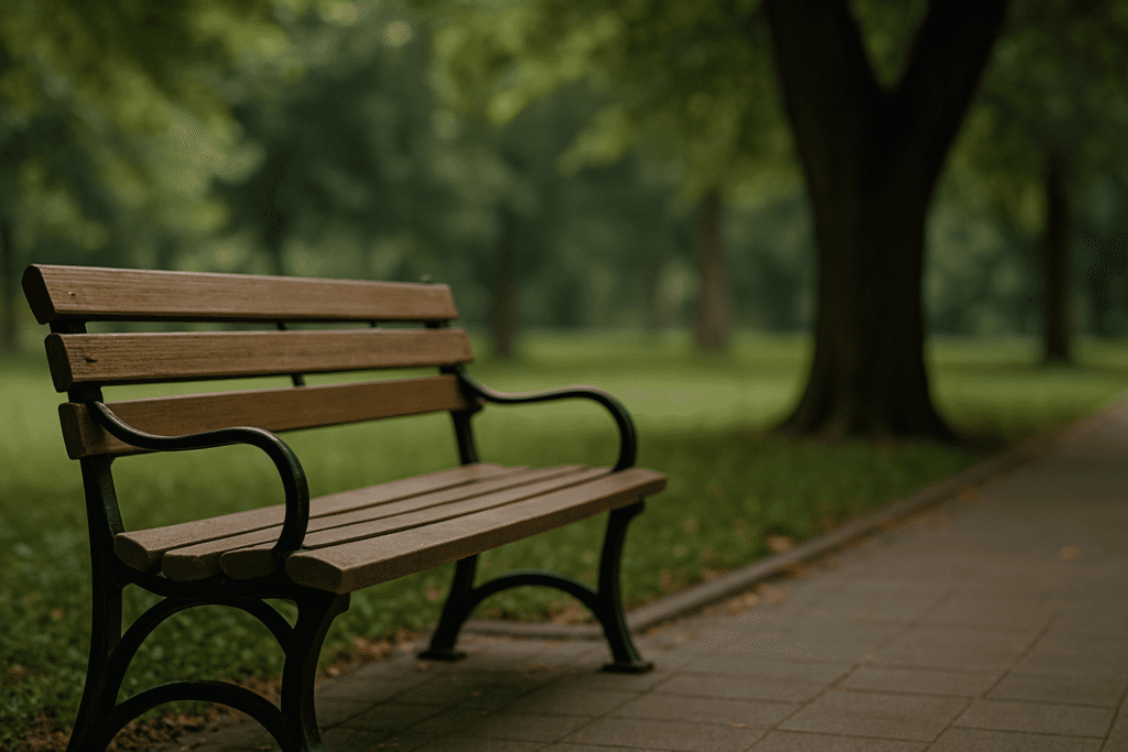 A wooden bench sits empty on a quiet park path beneath dappled sunlight from overhead trees, with soft greenery in the background