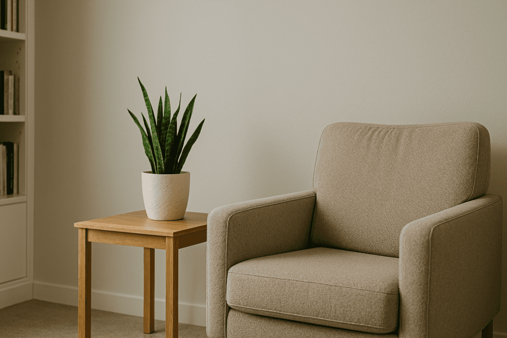 A peaceful therapy room corner with a beige armchair, snake plant, and natural light streaming across a neutral, calming space