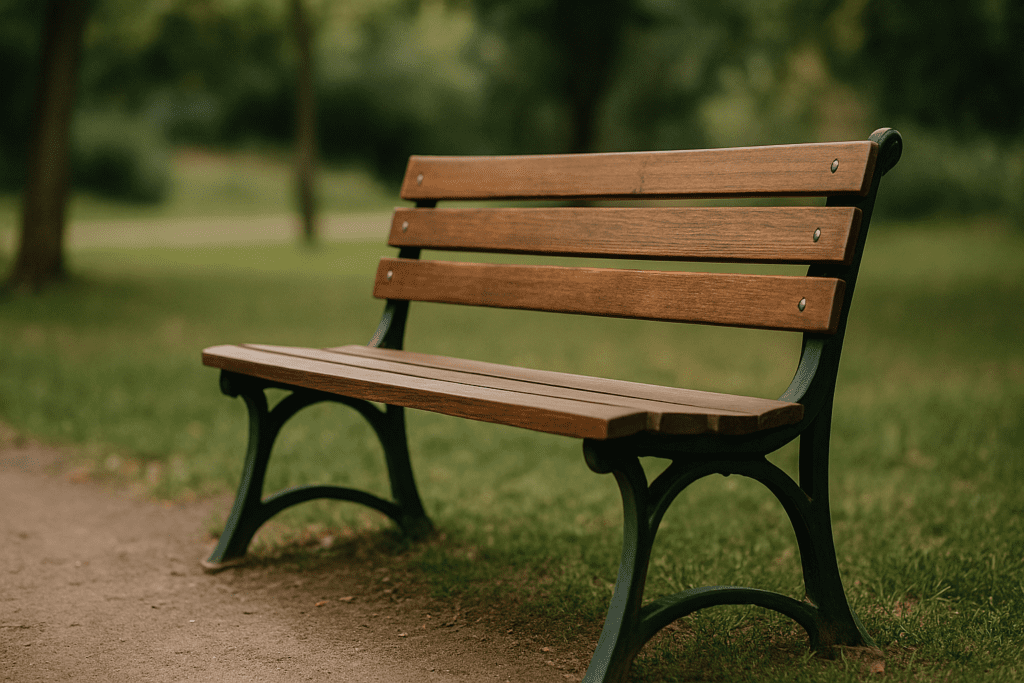  An empty wooden park bench with cast iron supports sits on a grassy path, surrounded by trees and soft afternoon sunlight